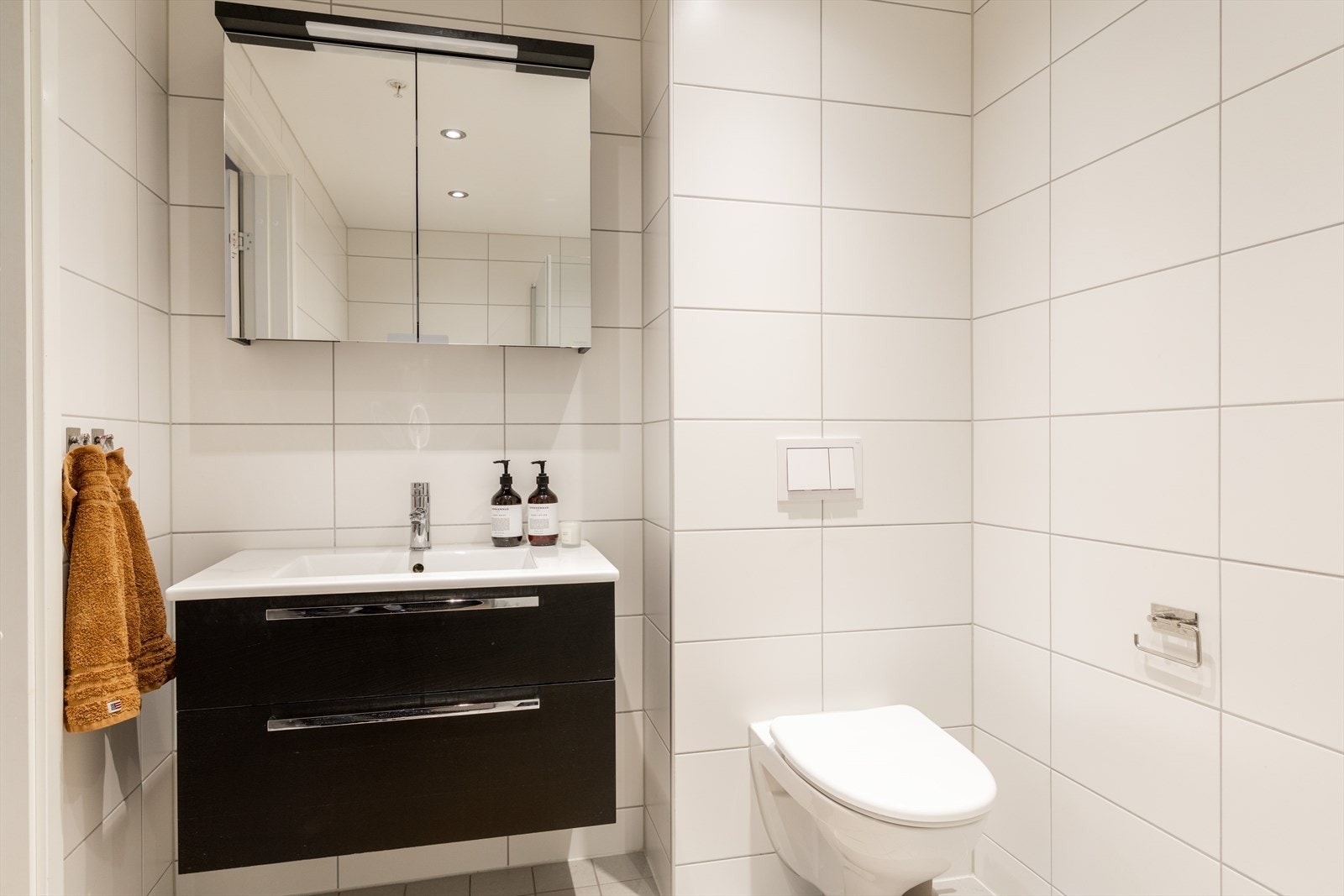 Badet er innredet med med vegghengt klosett, servant nedfelt i innredning, speilskap m/lys og dusjhjørne med svingbare glassdører. Galleribilde