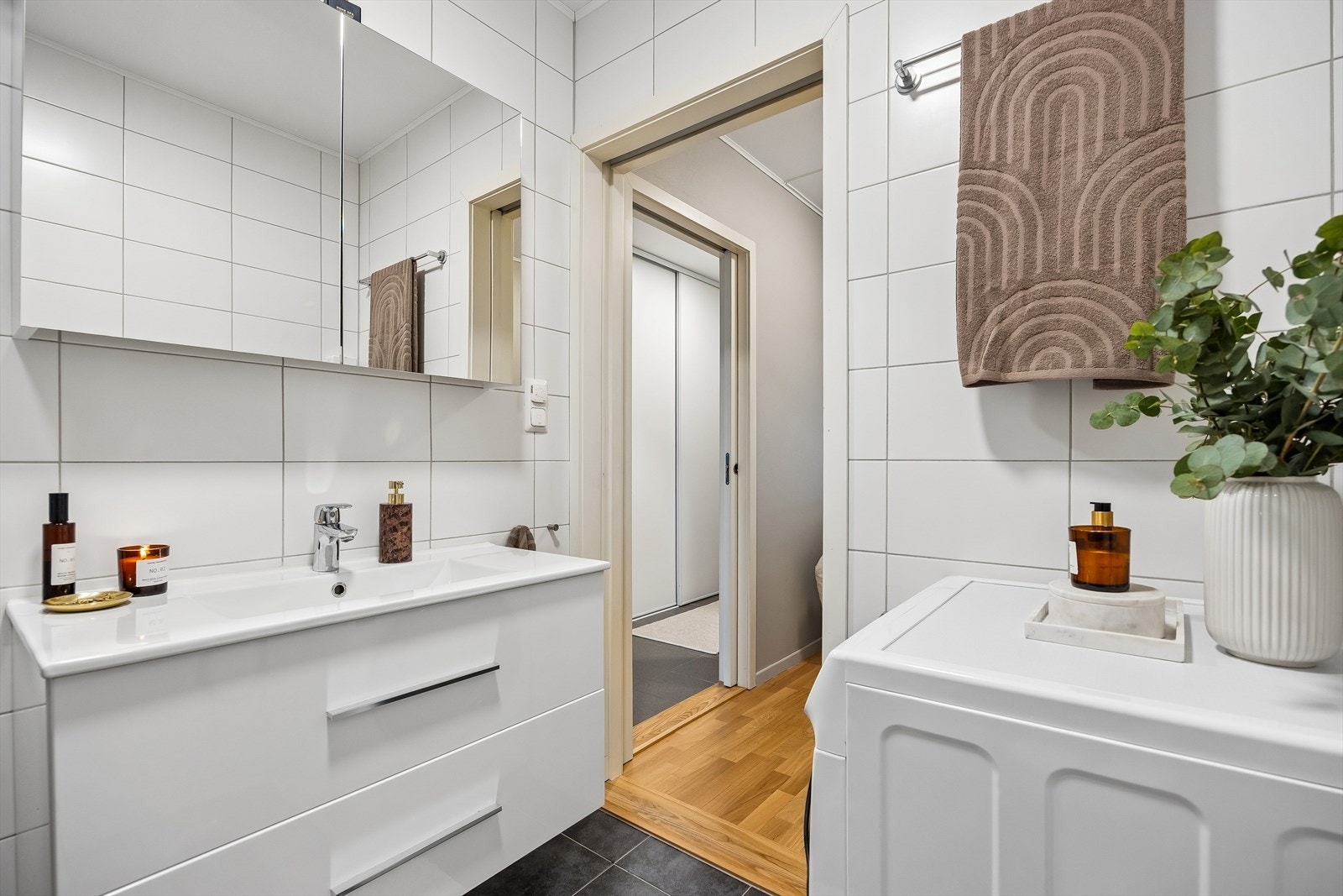 Badet er utstyrt med innfellbare dusjdører, mekanisk avtrekk, toalett, heldekkende servant med skuffer under, vegghengt speilskap, og opplegg for vaskemaskin/tørketrommel. Galleribilde