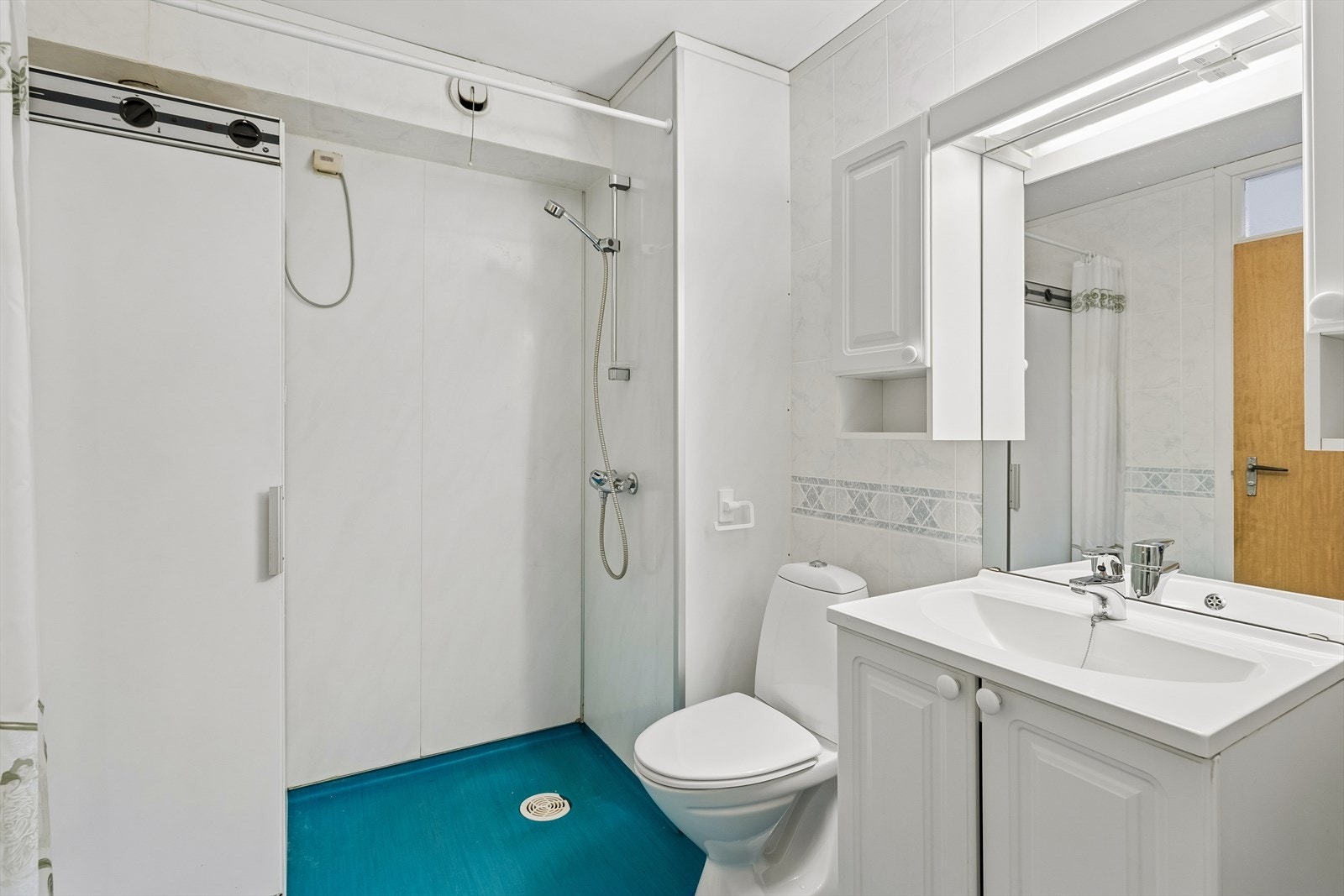 Badet har åpen dusjløsning, servant i skapinnredning, tørkeskap, skyllekum og opplegg for vaskemaskin. Galleribilde
