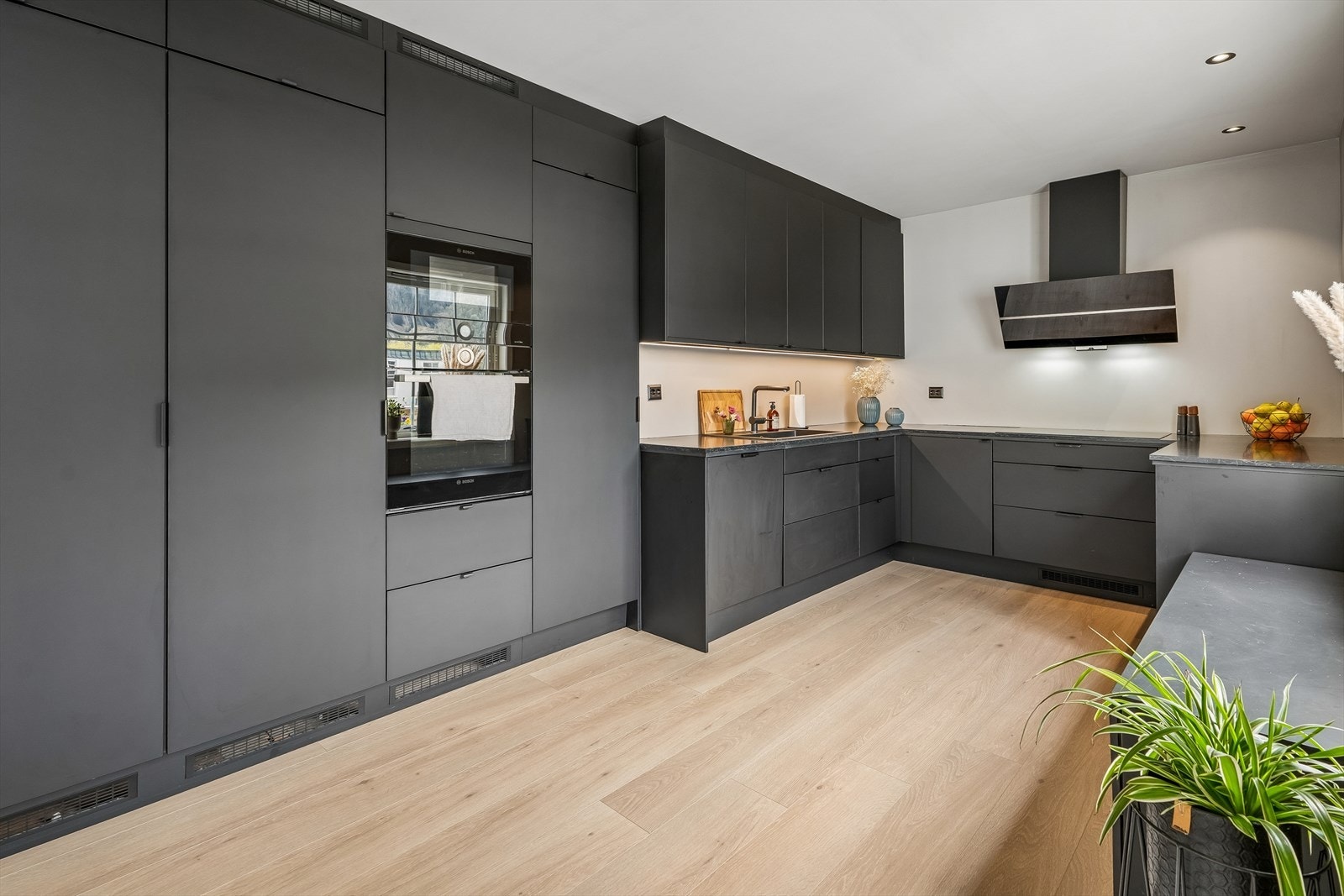 Stilreint og moderne kjøkken med mørke, slette frontar og rikeleg med skap- og benkeplass. Åpent mot spisestove og stove gjev deg eit meget godt allrom for familien Galleribilde