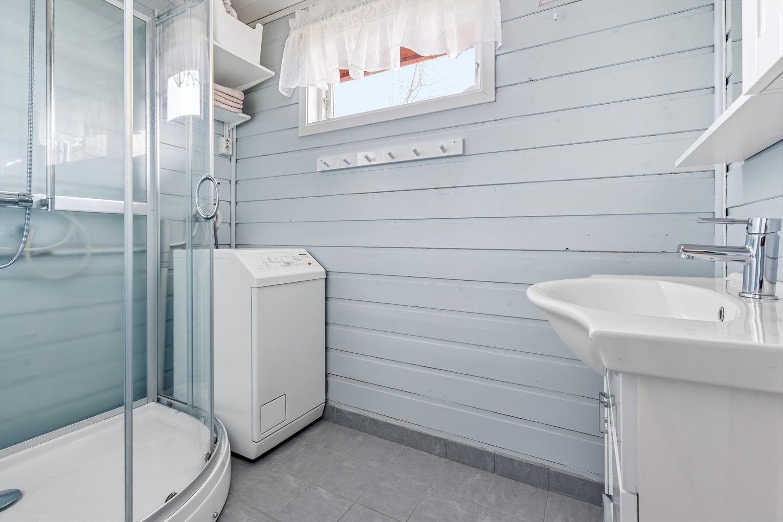Baderom i anneks med varmekabler i gulv, dusj og servant med skapinnredning. Opplegg for vaskemaskin er det også. Galleribilde