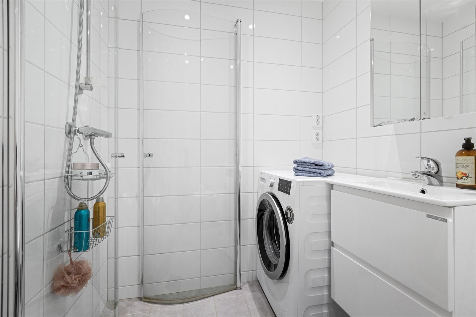Badet er flislagt og har vegghengt servantskap og wc, opplegg for vaskemaskin og dusjhjørne med svingbare glassdører. Galleribilde