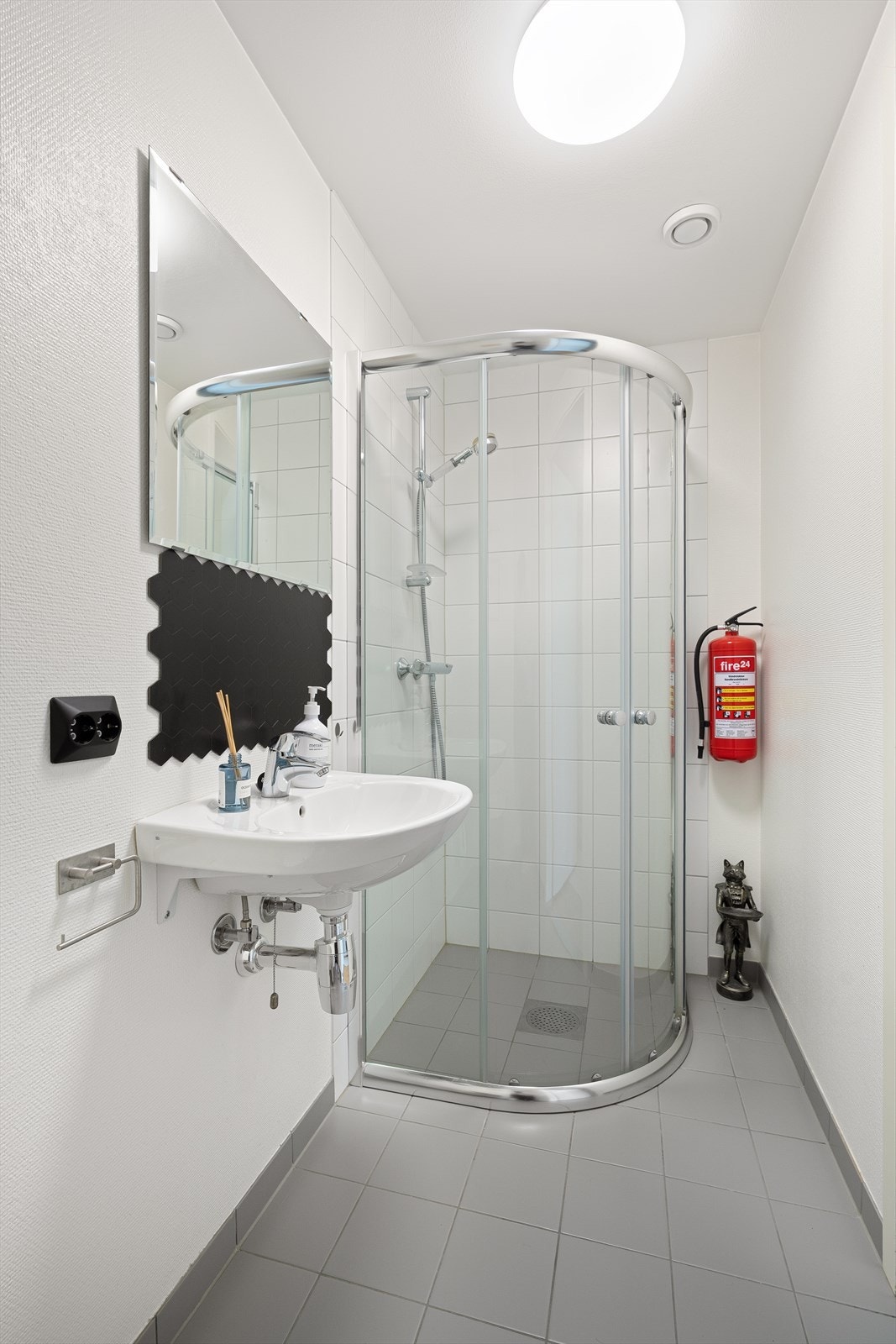 Praktisk bad i gang, med flis på gulv og i dusjsone. Badet har vegghengt toalett, servant og dusjhjørne. Galleribilde