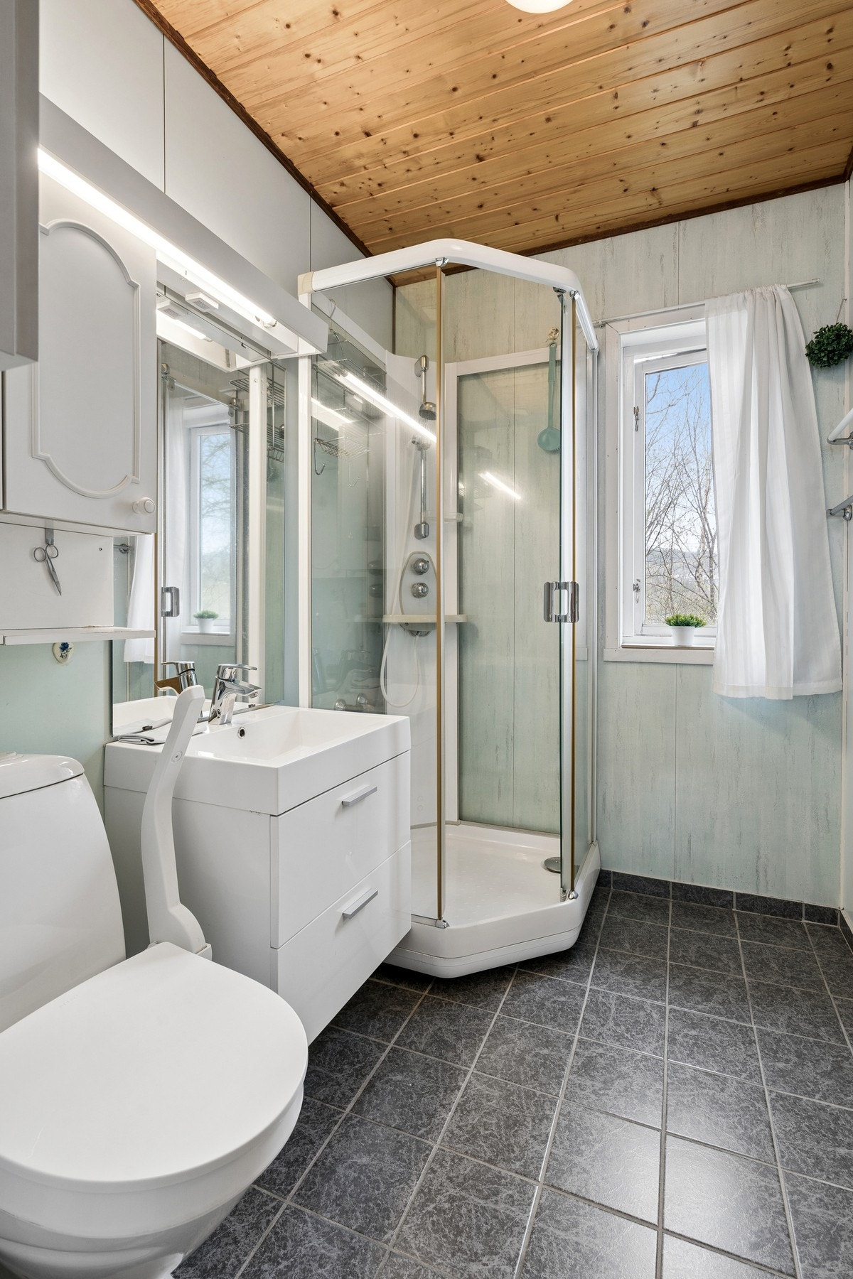 Badet i første etasje har fliser på gulv, baderomsplater på veggene og et praktisk dusjkabinett. Galleribilde