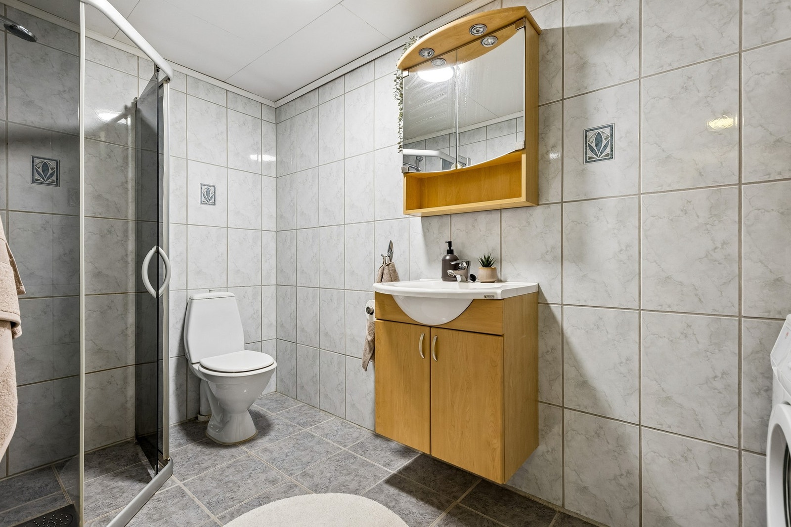 Badet på ca. 5 m² har flislagte overflater, gulvvarme og et praktisk dusjhjørne med dører. Galleribilde