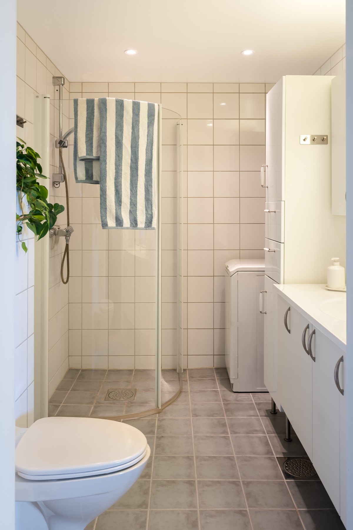 Her er hvit baderomsinnredning, høyskap, dusjhjørne med innfellbare glassdører, vegghengt toalett og opplegg for vaskemaskin/tørketrommel. Galleribilde