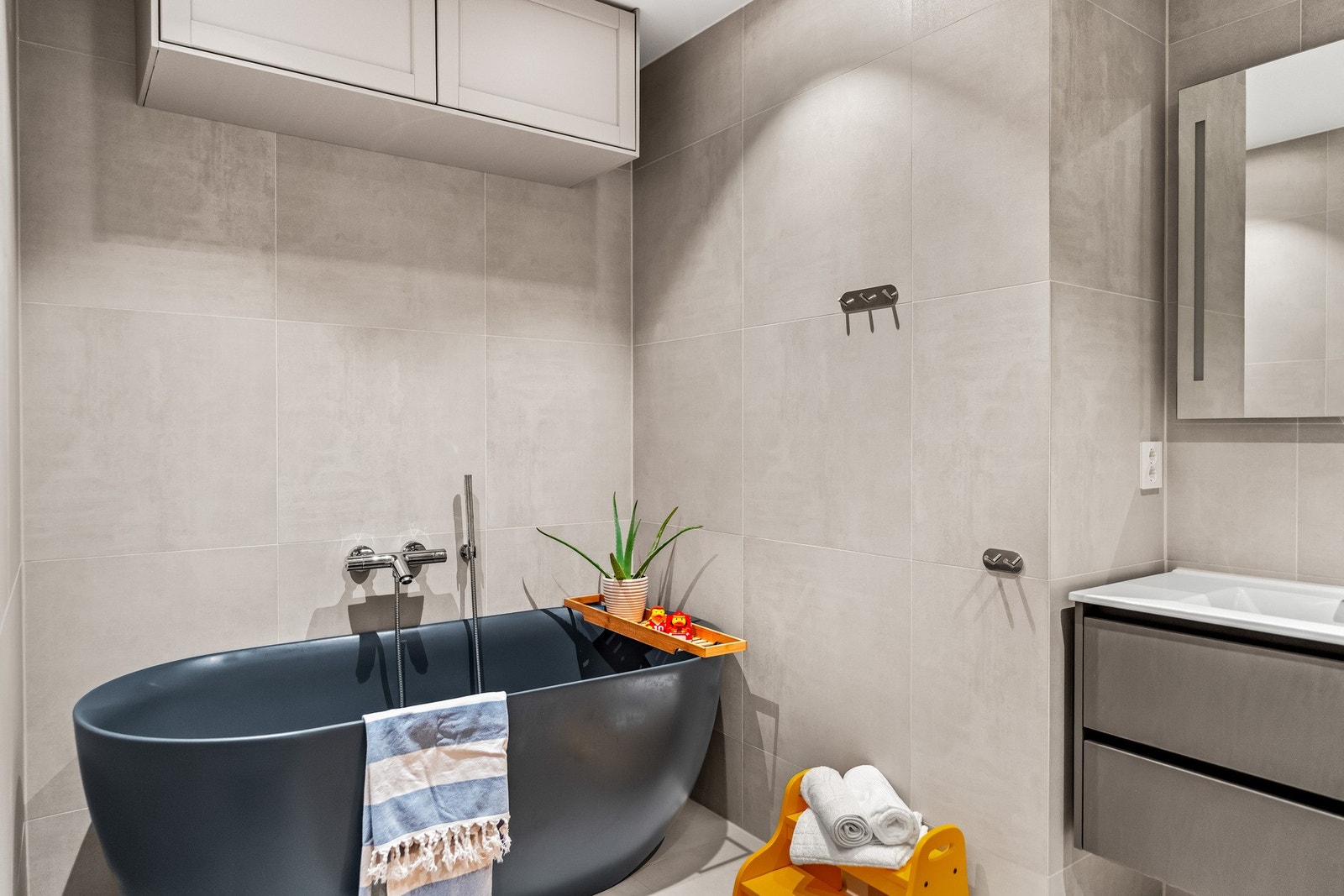 Badet fremstår som et lyst og innbydende rom med flislagte overflater, varmekabler og en komfortabel løsning med badekar som naturlig midtpunkt. Galleribilde
