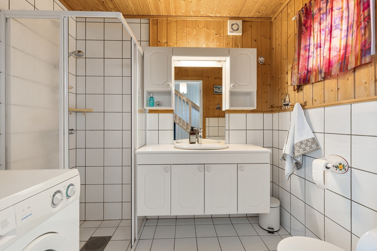 Praktisk bad med flislagte overflater og varmekabler. Rommet er innredet med dusjhjørne, opplegg for vaskemaskin, toalett og servant med tilhørende skap. Galleribilde