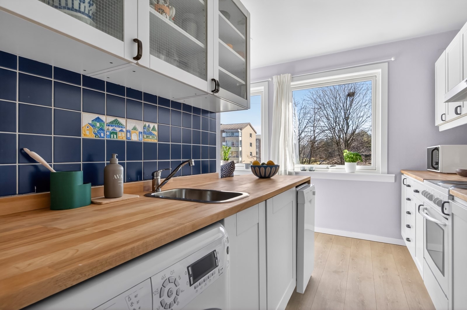 Kjøkkeninnredning med profilerte fronter og heltre benkeplate. Nisje til oppvaskmaskin, vaskemaskin, komfyr og kjøleskap. Galleribilde