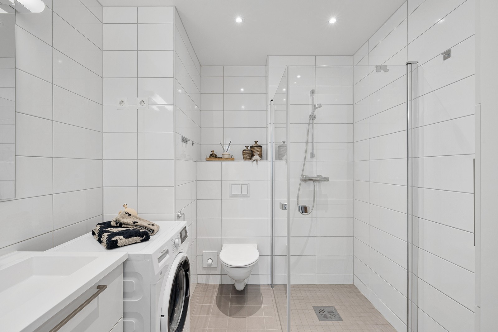 Badet har vegghengt skuffeseksjon med heldekkende servant, speil, dusjhjørne med glassdører, opplegg for vaskemaskin og vegghengt toalett. Galleribilde