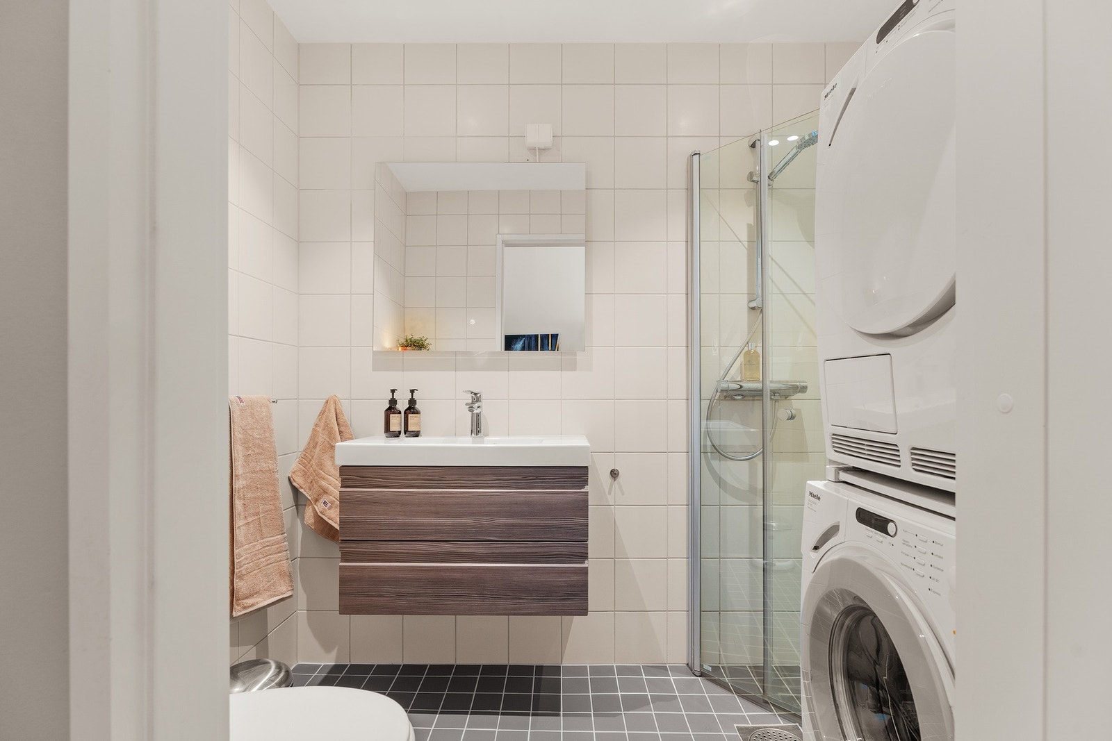 Det andre badet er også fra 2006, med flislagte overflater, og varmekabler i gulv. Rommet er utstyrt med servant med innredning, veggmontert toalett, dusjhjørne med glassvegger og opplegg for vaskemaskin. Galleribilde