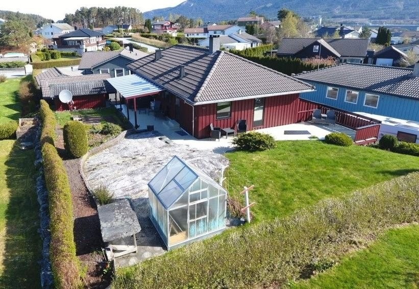 Oppsiden av boligen med oversikt over terrasse med tilhørende hage med drivhus og tørkehus. Galleribilde