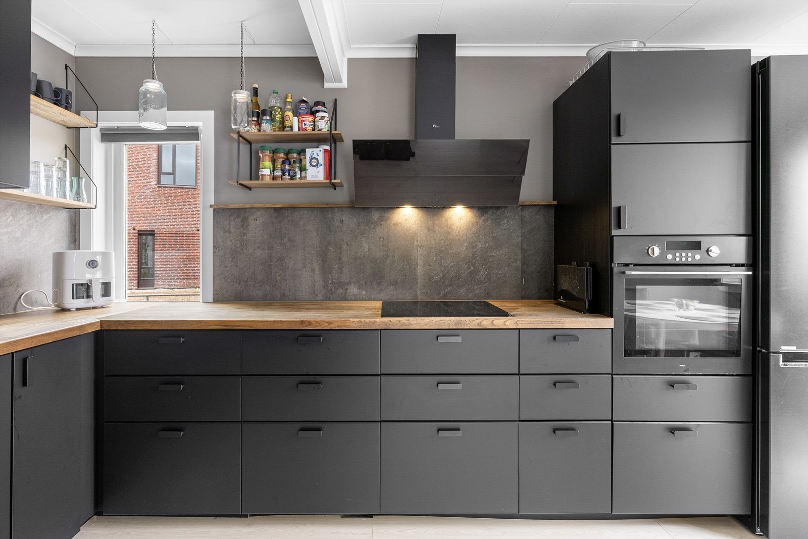 Kjøkkenet fremstår stilrent og gjennomført, med matte sorte fronter som gir et elegant og tidløst uttrykk, kombinert med en slitesterk laminatbenkeplate i tre. Galleribilde