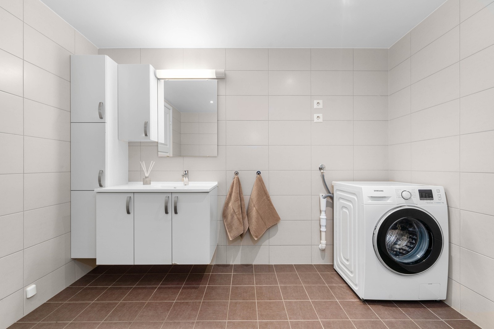 Flislagt bad med moderne trekk og lyse farger. Badet er stort med god plass for oppbevaring og opplegg for vaskemaskin. Galleribilde