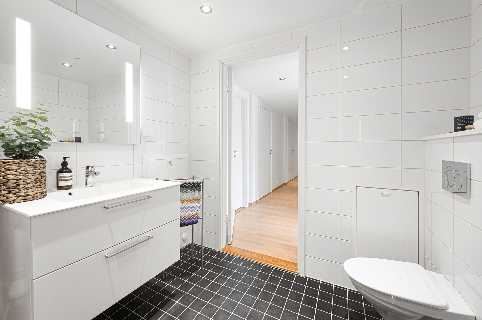 Badet er innredet med dusjhjørne med innfellbare dusjdører i glass, opplegg for vaskemaskin, vegghengt WC, servant på underskap, og speil. Galleribilde