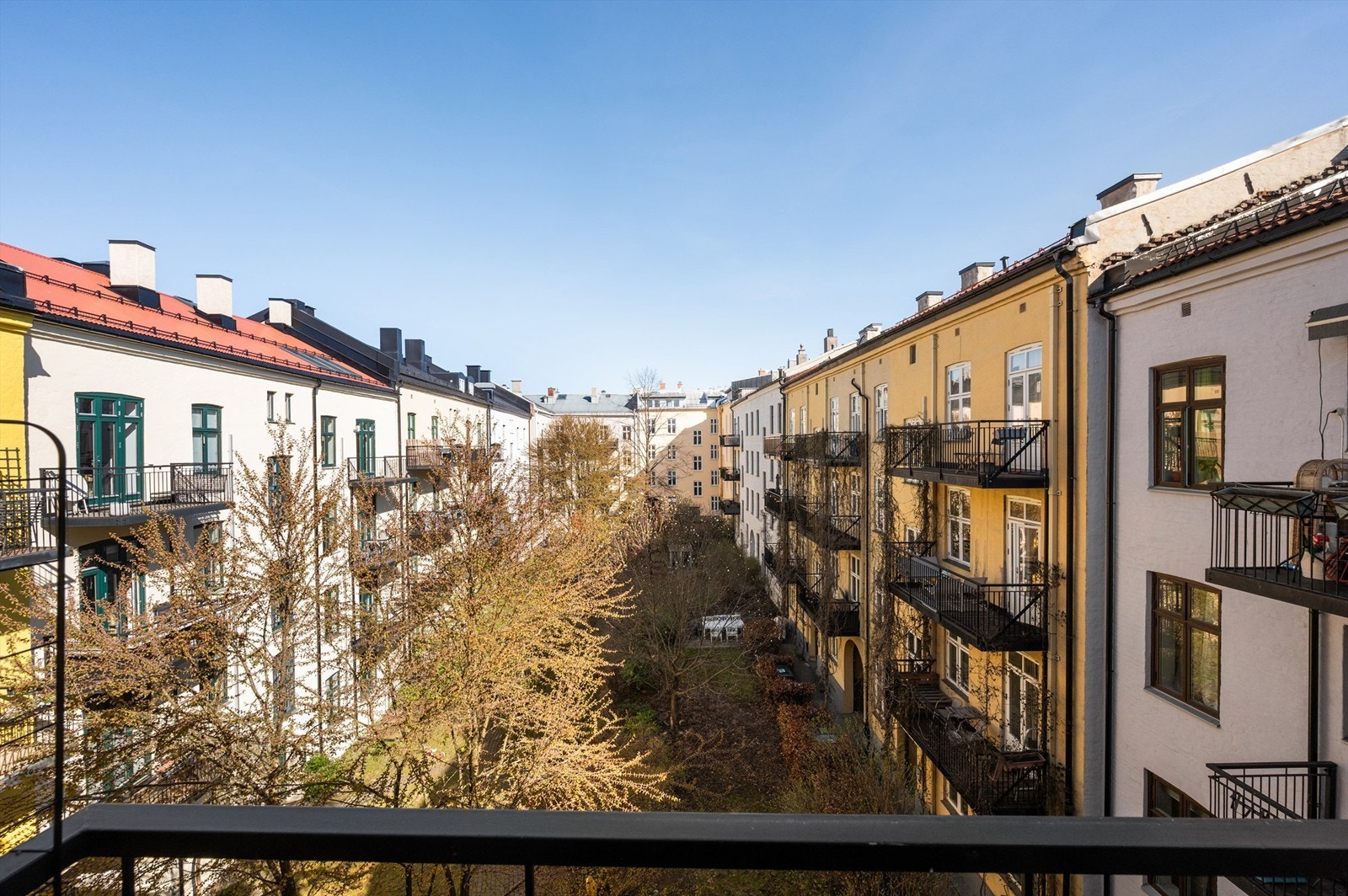 Utsikt fra balkongen mot den skjermede og grønne bakgården, et fellesareal som gir en rolig kontrast til det pulserende livet i Markveien. Galleribilde