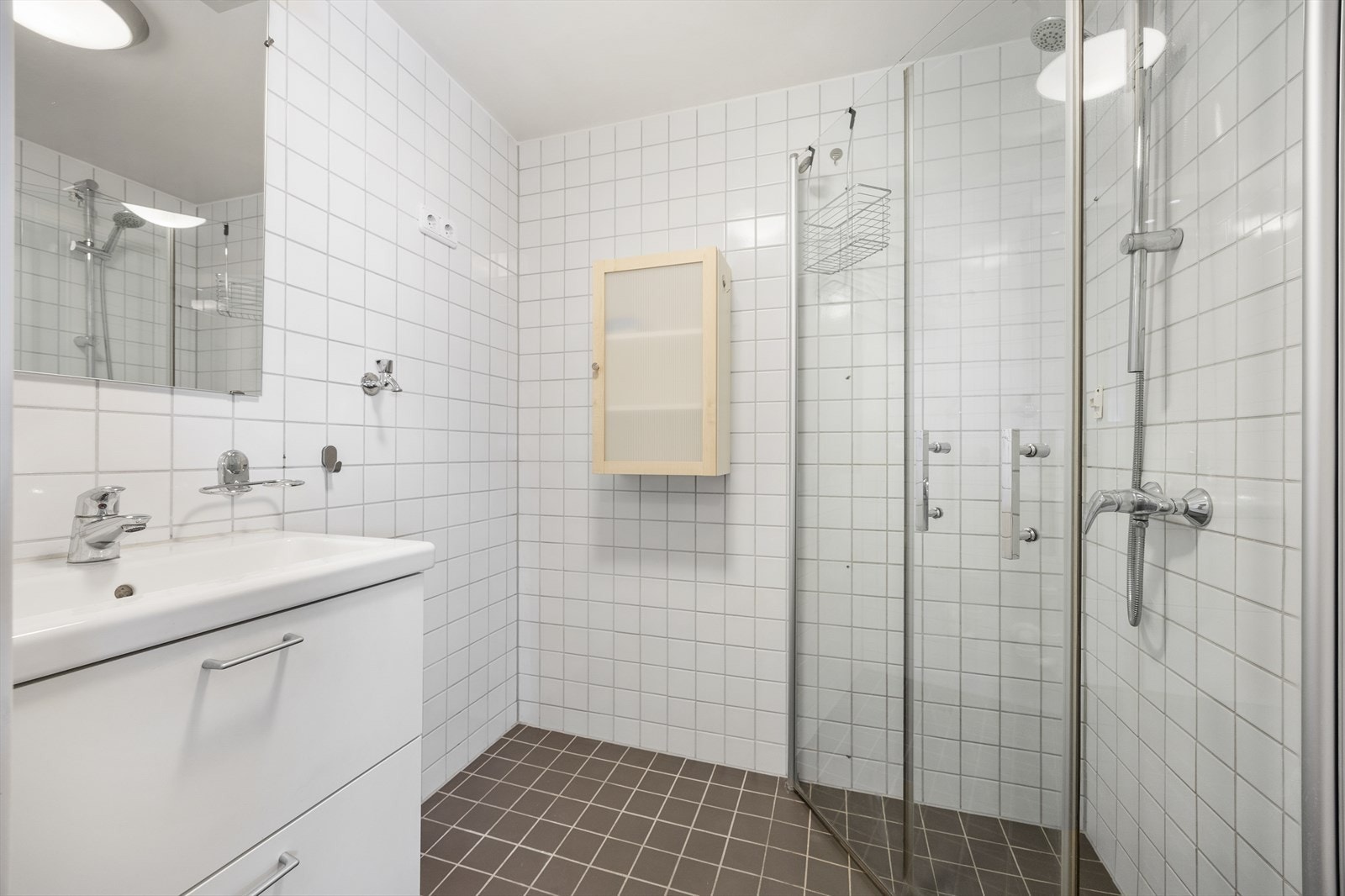 Badet er flislagt og har elektriske varmekabler i gulvet. Dusjhjørnet har praktiske, innsvingbare glassdører. Galleribilde