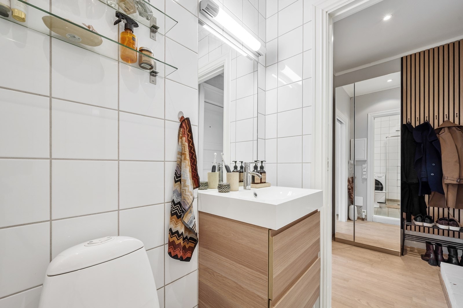 Innredningen består av gulvstående toalett, servant med skuffeinnredning, speil på vegg med belysning, dusjhjørne med glassdører og opplegg for vaskemaskin. Galleribilde