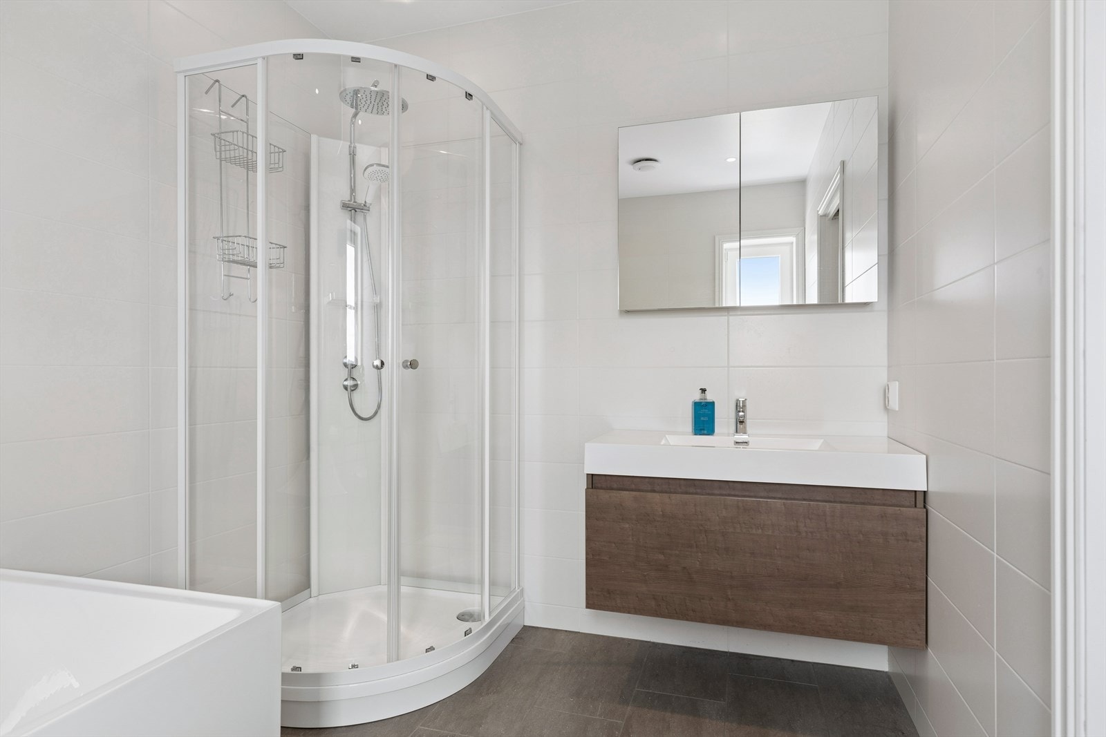 Tidsriktig, helfliset baderom med elektriske varmekabler i gulv. Taket er malt. Badet er utstyrt med innredning med nedfelt servant, veggmontert toalett, badekar og dusjkabinett. Galleribilde