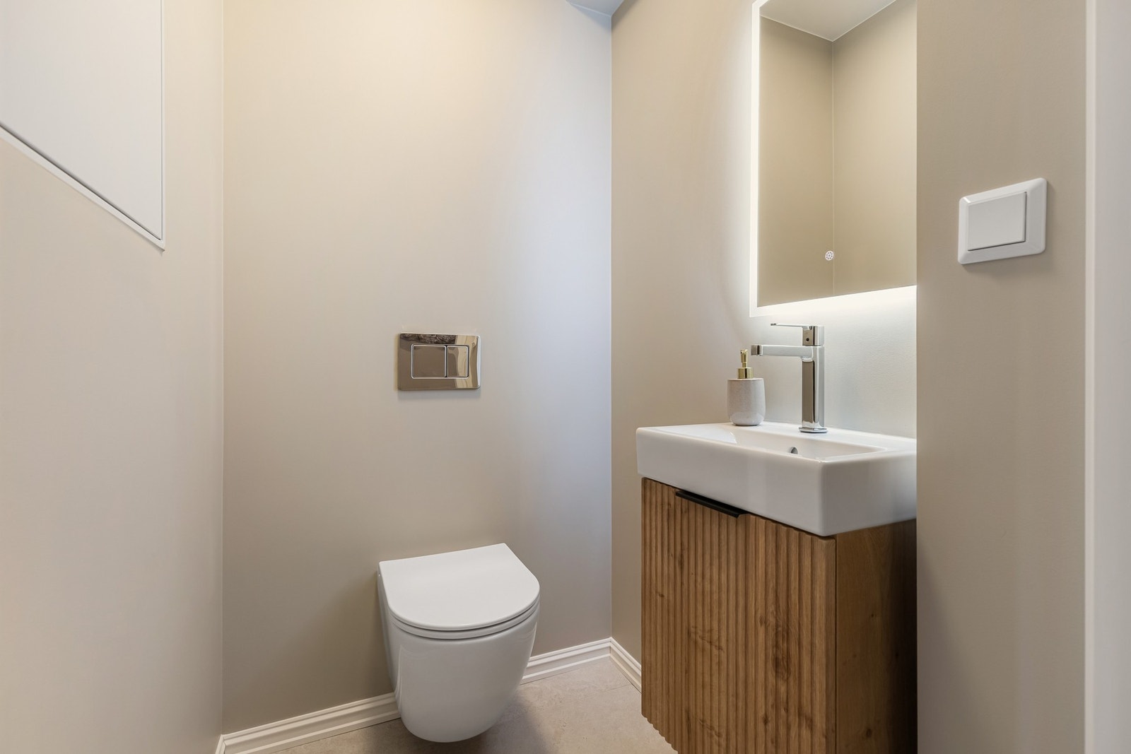 Praktisk og stilrent WC-rom med flislagt gulv, enkel servant med underskap og speil med integrert belysning. Galleribilde
