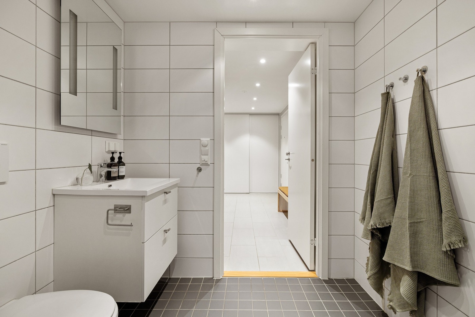 Baderommet har mørke fliser på gulv, elektrisk gulvvarme, hvite fliser på veggene, downlights i himlingen og mekanisk avtrekksvifte. Galleribilde