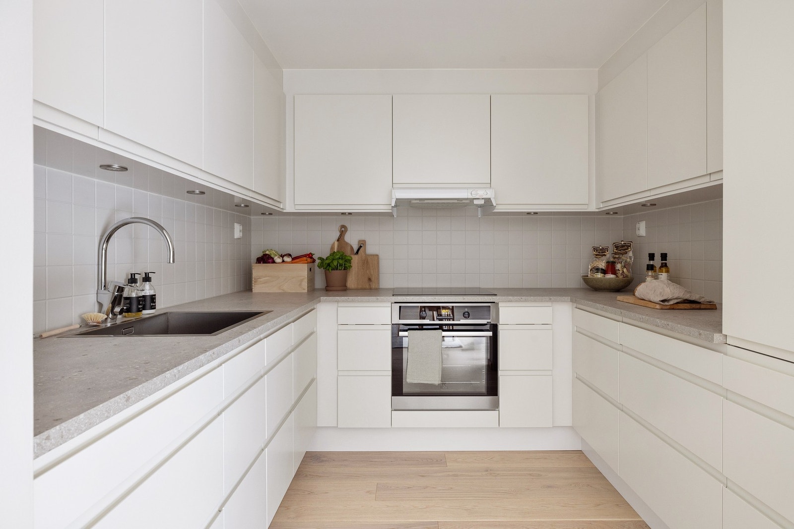 Innredningen har hvite glatte fronter og laminert benkeplate med nedfelt oppvaskkum. Praktisk med fliser i benkeryggen og belysning under de takhøye overskapene. Galleribilde