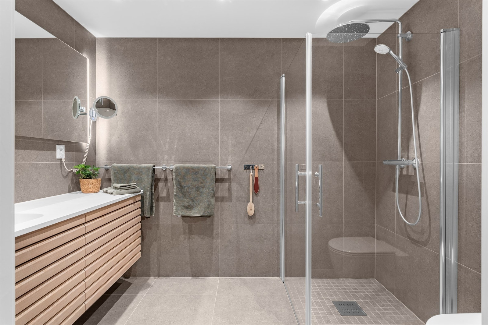 Badet har dusjnisje med glassdører og ett-greps dusjarmatur. Vegghengt toalett med innebygget sisterne. Galleribilde