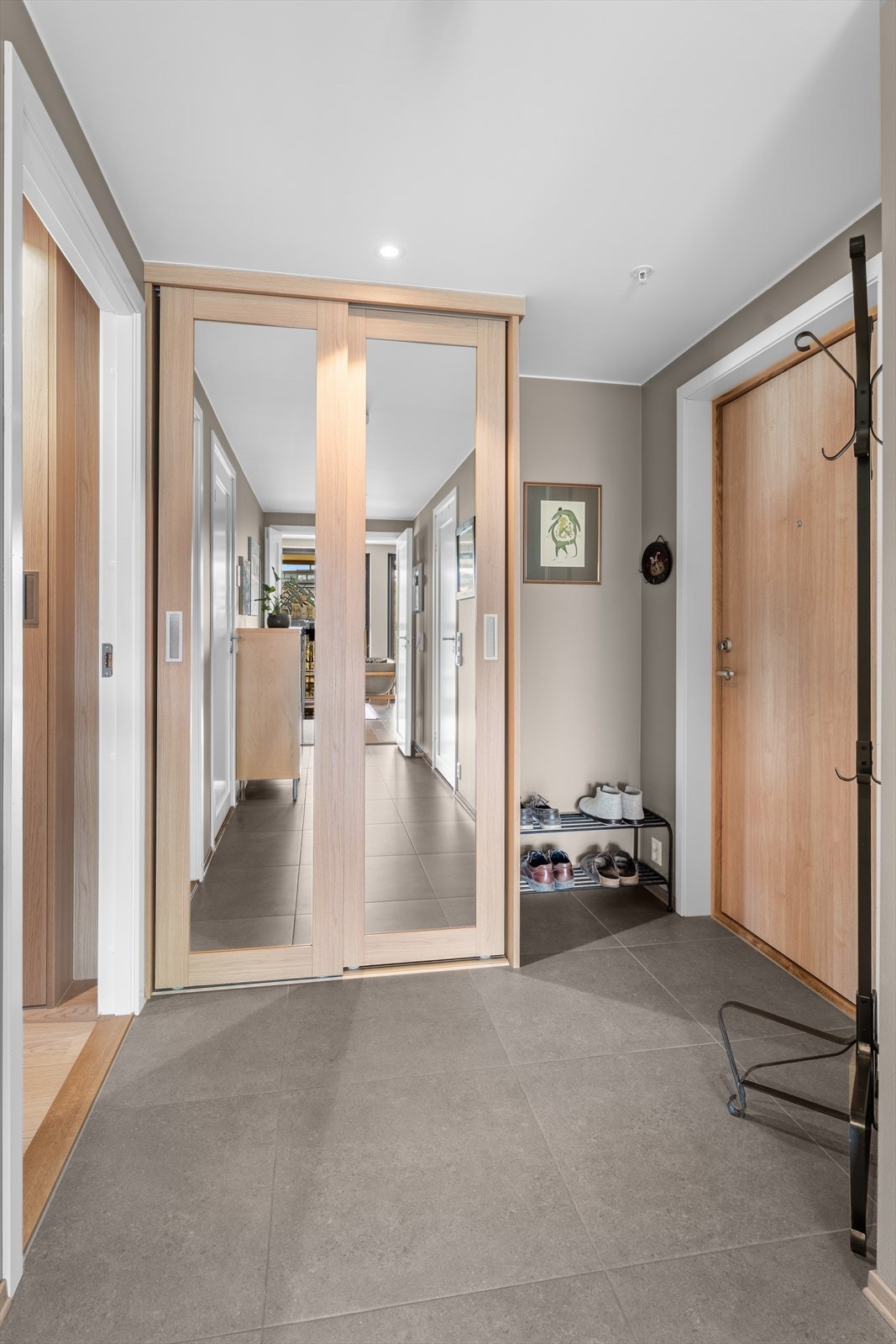 Pen entré med fliser på gulv og downlights i tak. Praktisk skyvedørsgarderobe for oppbevaring av yttertøy og sko. Gulvvarme Galleribilde