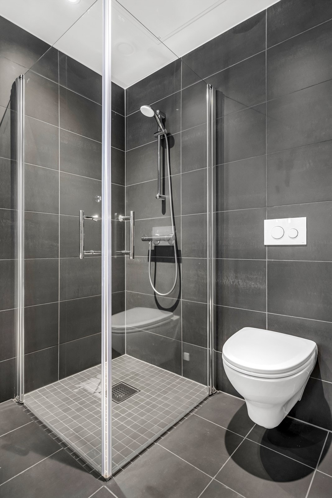 Badet er utført i moderne og stilrene fliser med behagelig gulvvarme. Innredningen består av servantskap med skuffeseksjon, nedfelt servant, speilskap, vegghengt toalett og dusjhjørne med glassdører. Galleribilde