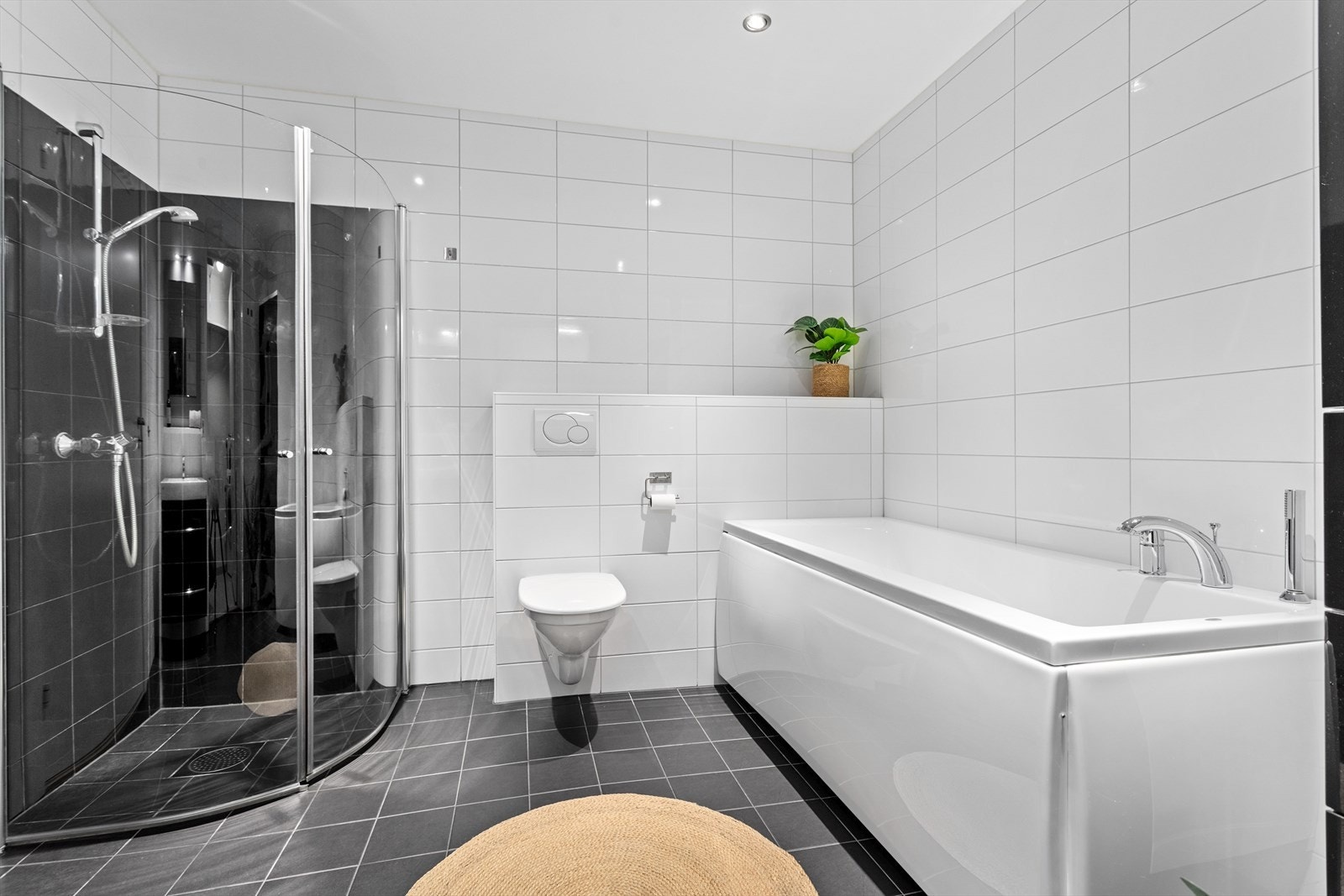 Badet er utstyrt med veggmontert toalett, badekar, dusjnisje med boga glasdører, servantskap med skuffer i svart høgglans og heilskøytt servant, samt eit høgskap i same utføring. Galleribilde