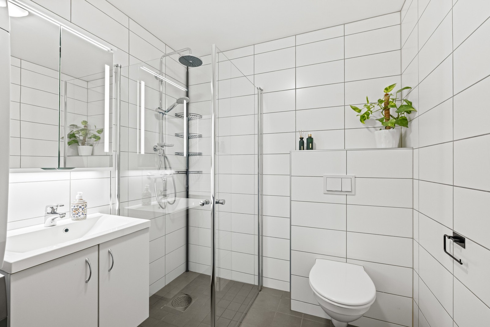 Badet fremstår som stilrent med grå fliser på gulv og hvite fliser på vegger, med gulvvarme som gir god komfort i hverdagen. Galleribilde
