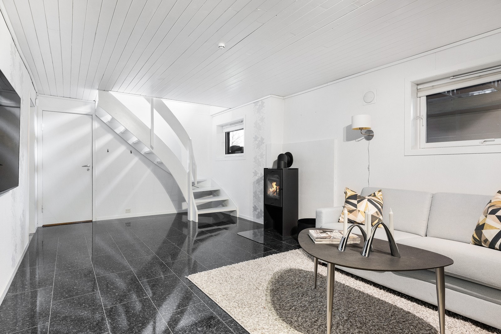 En trapp ned er en kjekk kjellerstue med fliser og gulvvarme, samt vedovn. Galleribilde