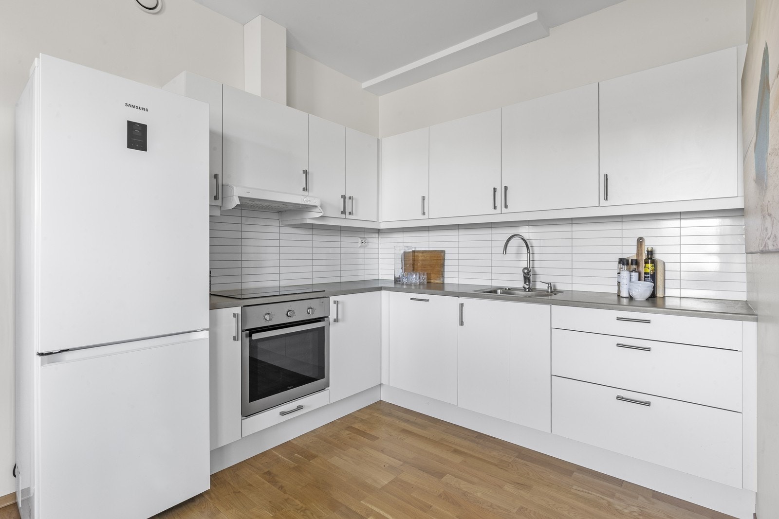 Kjøkkeninnredning med glatte fronter og laminatbenkeplate. Kjøkkenet er utstyrt med platetopp, stekeovn og kjøl/fryseskap. Galleribilde
