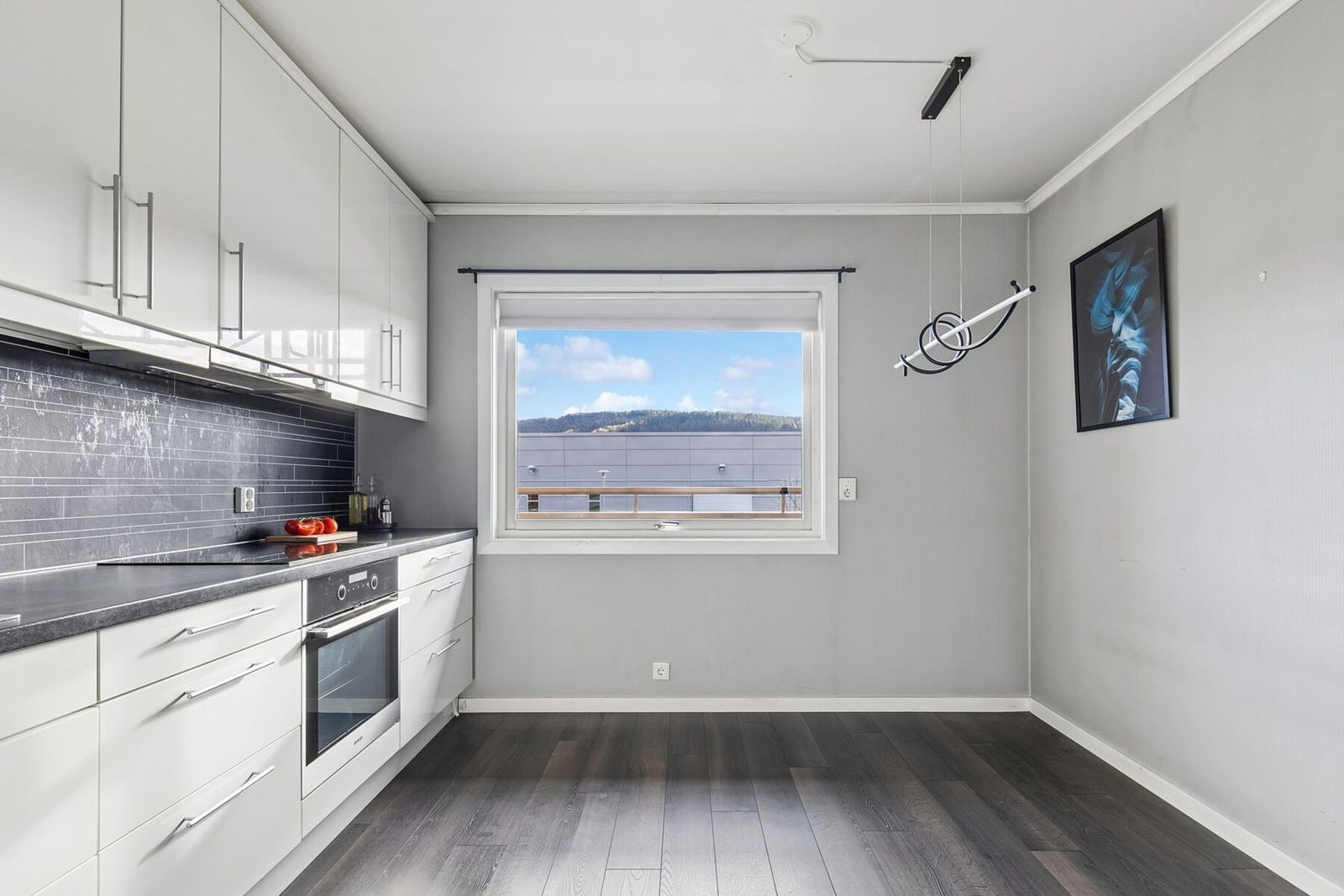 Kjøkkeninnredningen er utstyrt med hvite, glatte fronter og benkeplate i laminat med nedfelt kum i rustfritt stål. Galleribilde