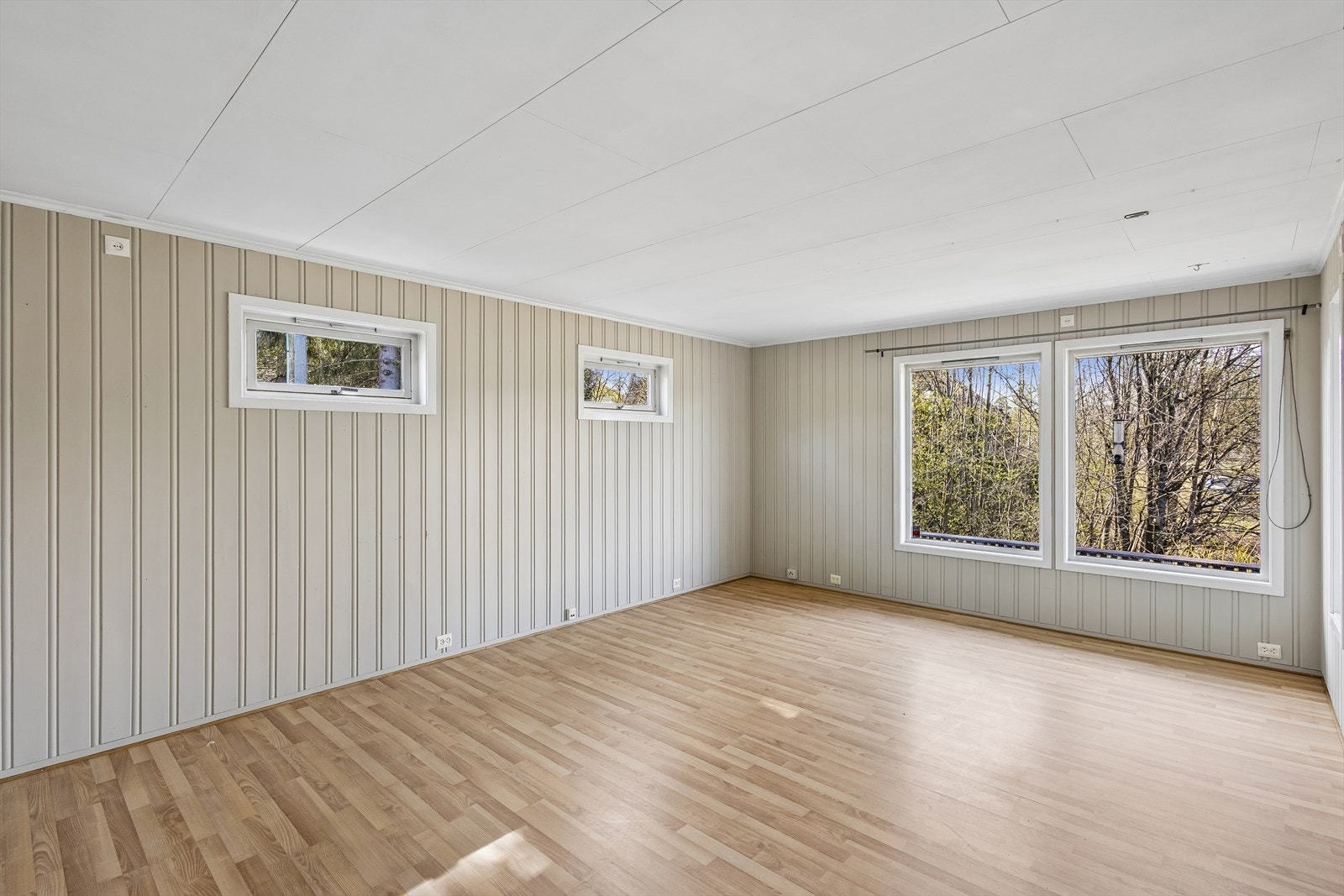 Overflatene i stuen består hovedsakelig av laminat på gulv og malt trepanel på veggene. Galleribilde