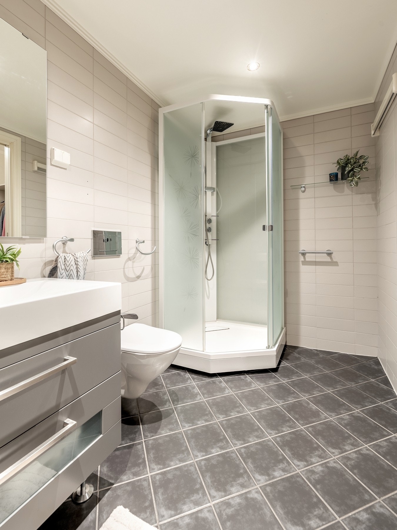 Badet er innredet med servantinnredning, speil på vegg over servant, ett høyskap, vegghengt toalett og dusjkabinett. Galleribilde