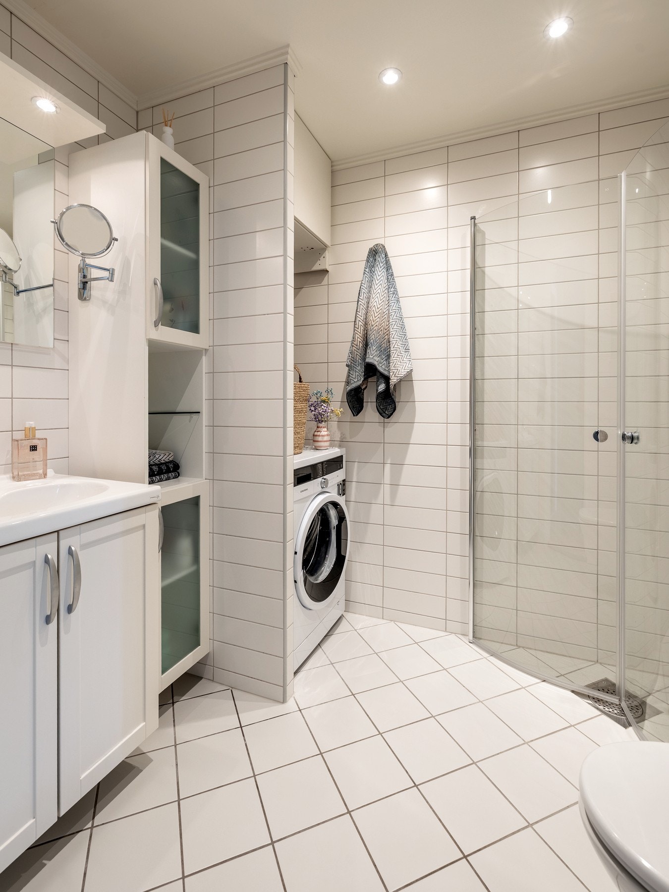 Badet er innredet med servantinnredning, speil på vegg over servant, ett høyskap, vegghengt toalett, dusjhjørne med svingbare glassdører og opplegg for vaskemaskin. Galleribilde