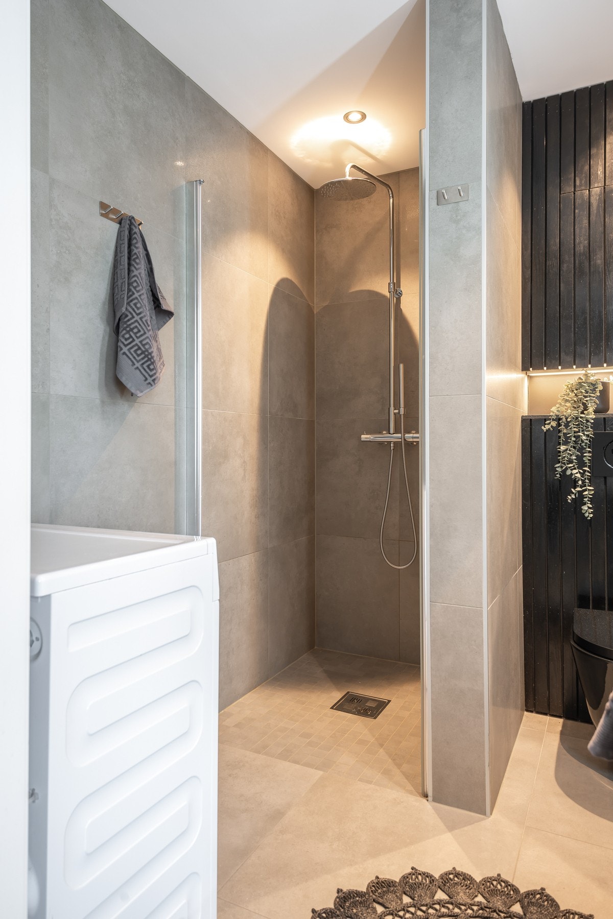 Egen dusjnisje med waterfall dusj, vegghengt toalett, sort innredning med servant og opplegg for vaskemaskin. Galleribilde