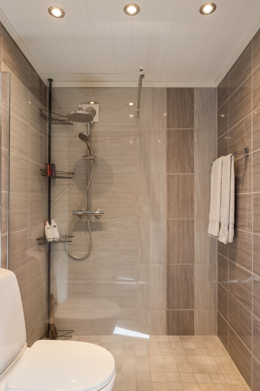 Badet har gulvmontert toalett og dusjhjørne med veggmontert dusjbatteri med regnfall. Galleribilde