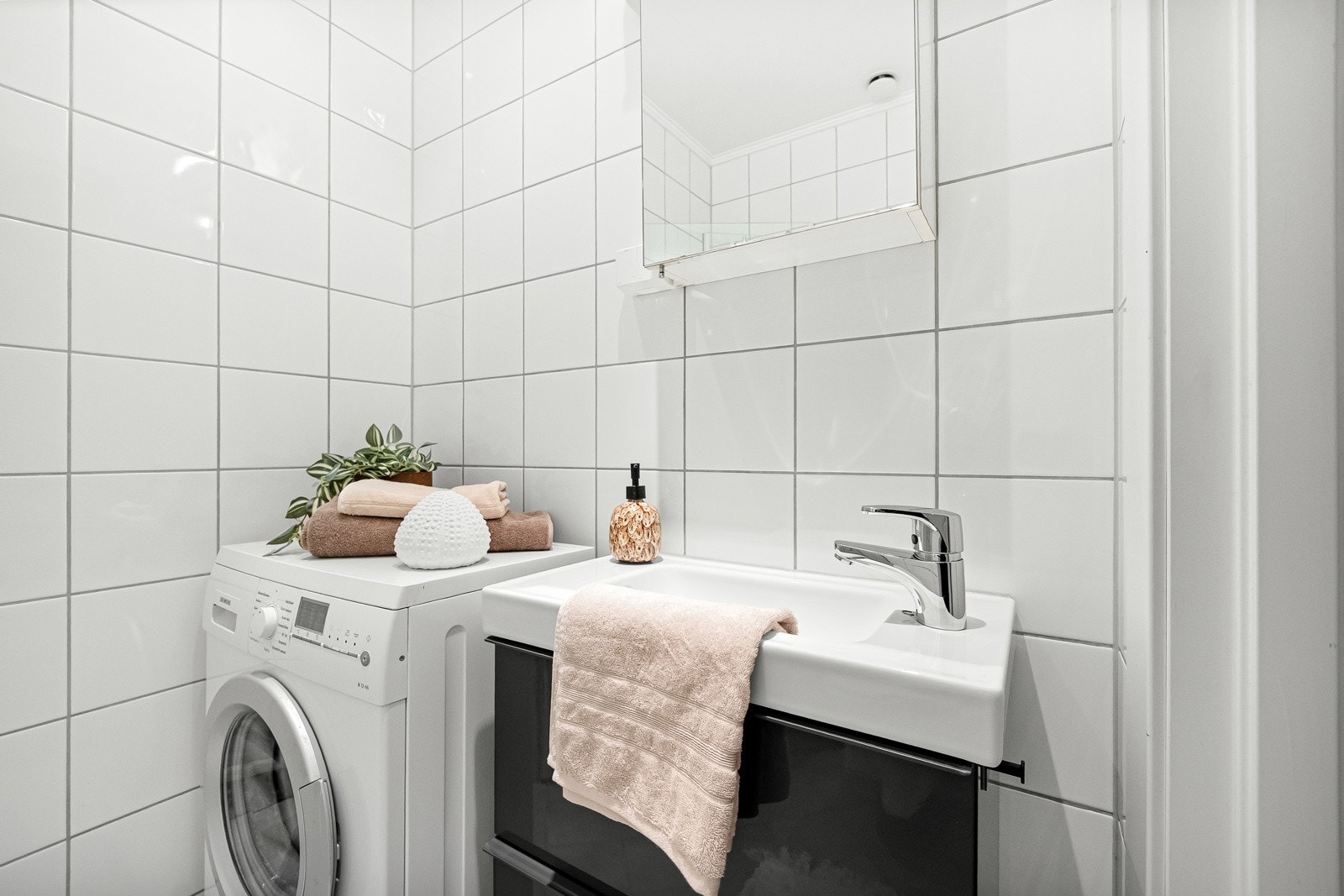 Badet er innredet med servantskap med glatte, høyglans fronter og heldekkende servant, speilskap med lysarmatur over servant, veggmontert klosett og dusjhjørne med svingdører, sluk og termostatstyrt blandebatteri. Galleribilde