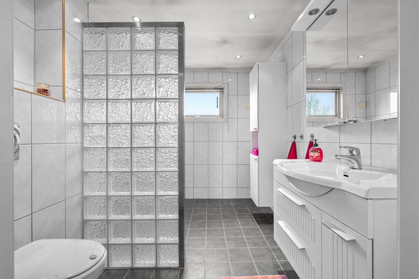Flislagt bad med varmekabler. Badet har benke- og overskap med fronter, overskap med speilfronter. Videre har badet servant, veggfestet klosett, dusj på gulv og opplegg for vaskemaskin. Galleribilde