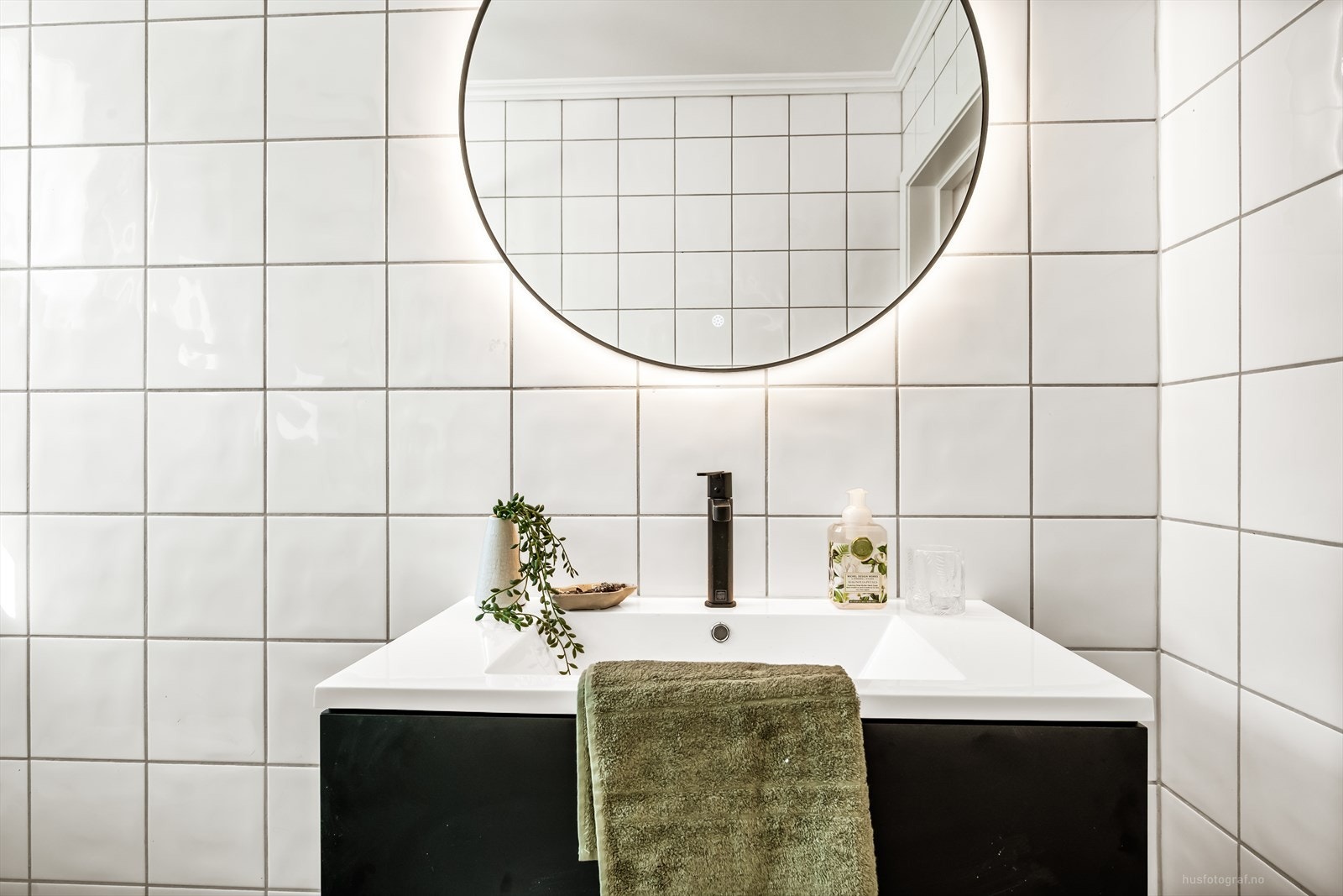 Baderomsinnredning med nedfelt servant og et stort, rundt speil med integrert belysning. Galleribilde