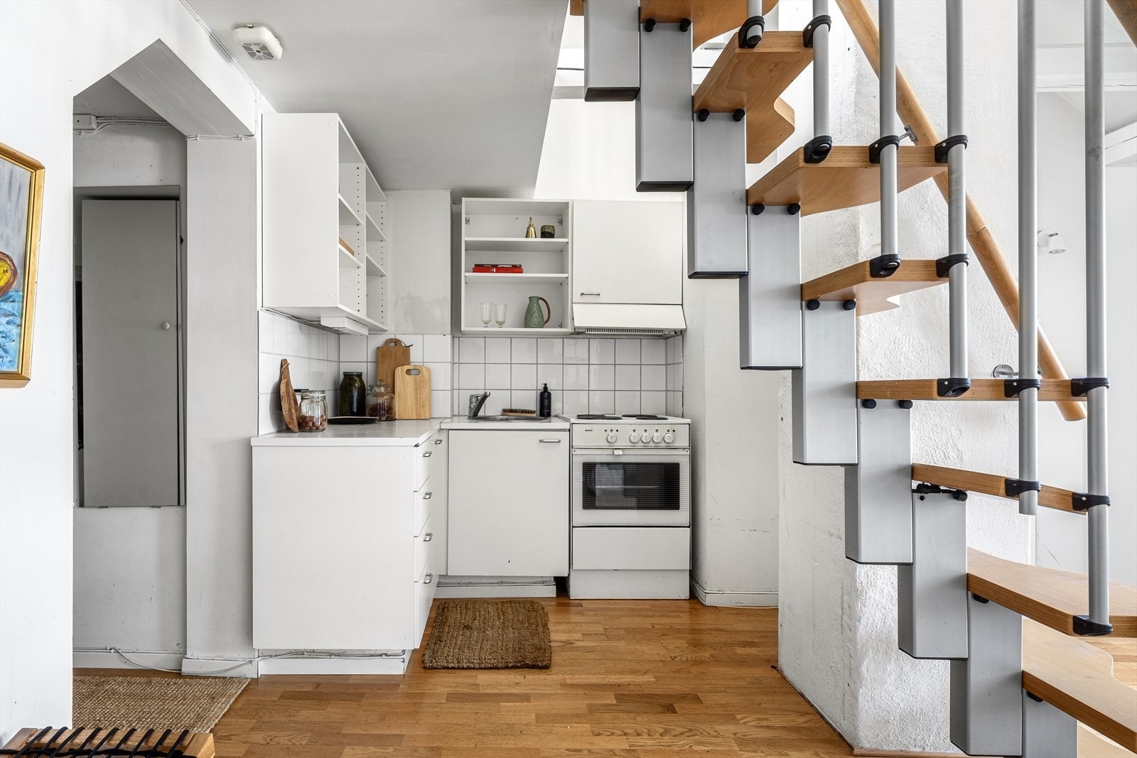 Kjøkkeninnredning med slette fronter og fliser med belysning over malt laminat benkeplate. Det er ventilator over koketopp med kullfilter. Galleribilde
