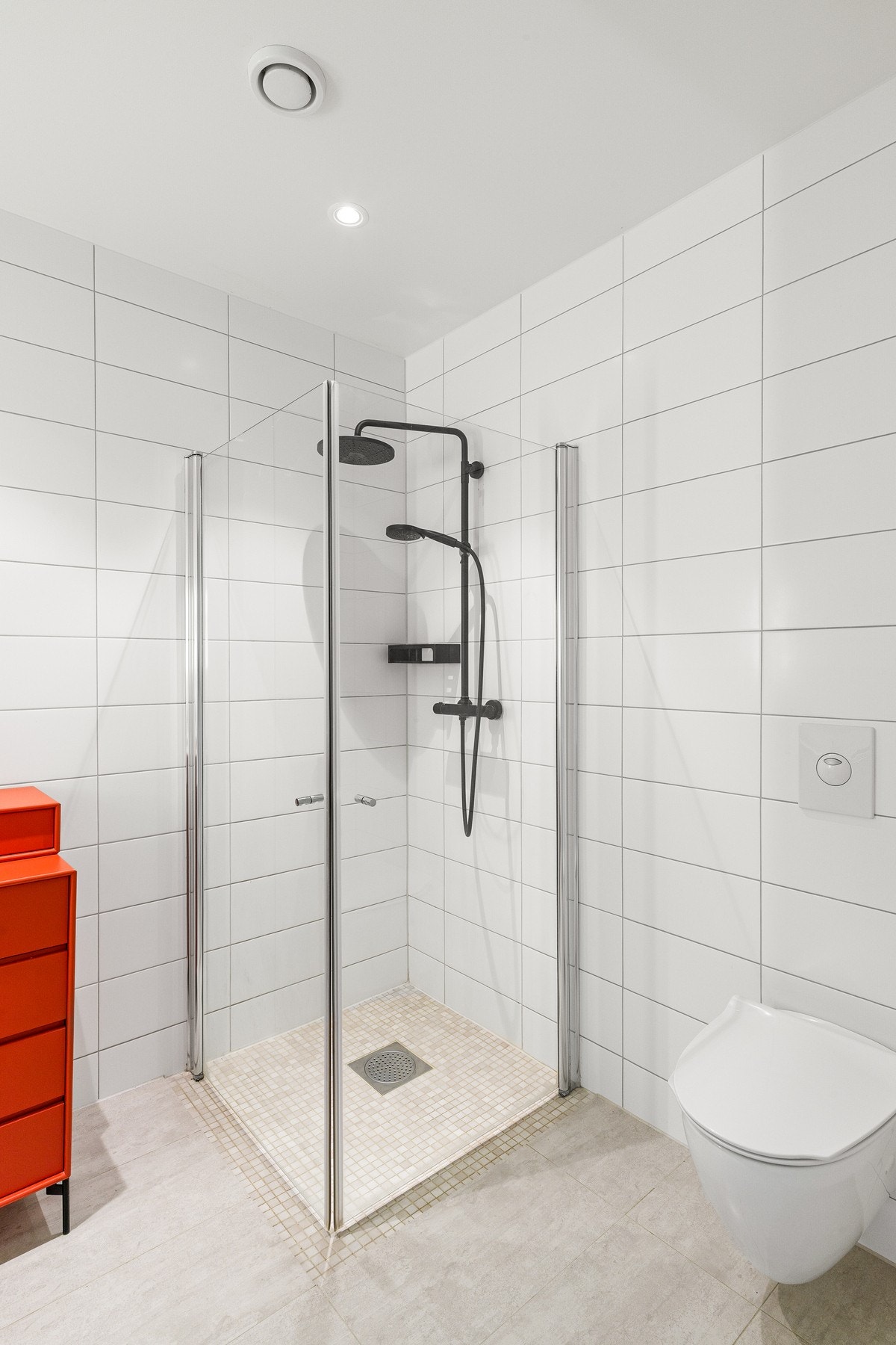 Badet er innredet med dusjhjørne i glass, vegghengt toalett og hvit baderomsinnredning med tilhørende speil med lys. Galleribilde