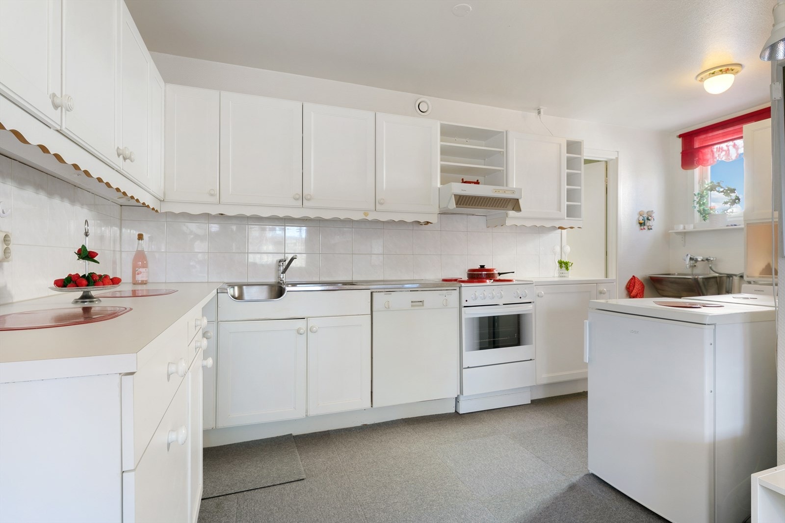 Kjøkkeninnredning fremstår med profilerte malte fronter. Laminert benkeplate oppvaskkum i benkebeslag og 1-greps blandebatteri. Lys under overskap, ventilator med kullfilter. Det er opplegg for oppvaskmaskin. Galleribilde