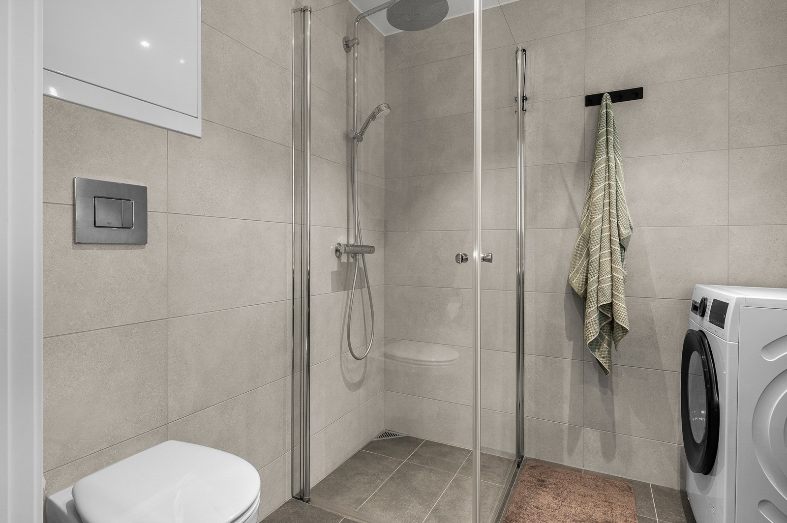 Badet er utstyrt med vegghengt toalett, hjørnedusj, baderomsinnredning og opplegg for vaskemaskin. Galleribilde
