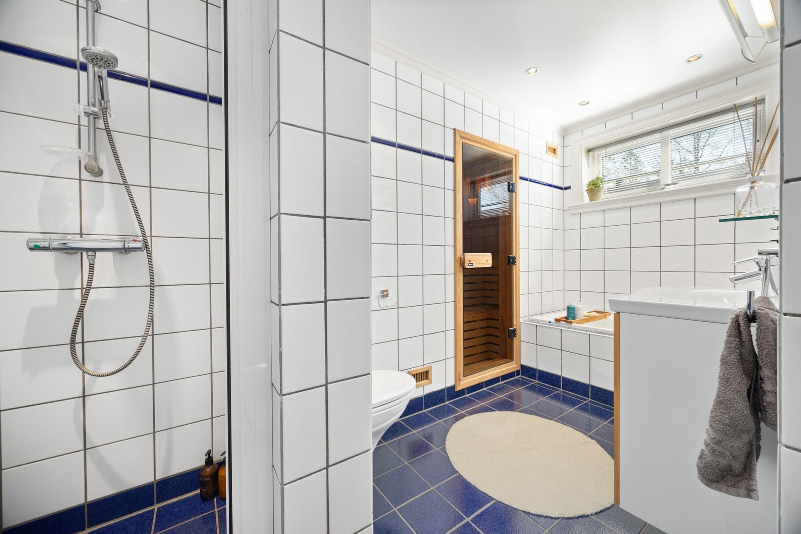 Badet har flislagte vegger og gulv, servant med underskap, speil med belysning og badekar. Galleribilde