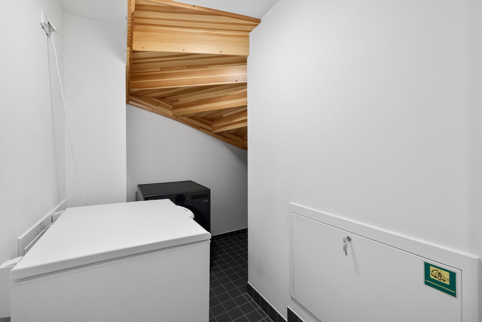 Under trappen finner du et vaskerom med flis på gulv, opplegg for vaskemaskin og rørfordelingsskap. Galleribilde
