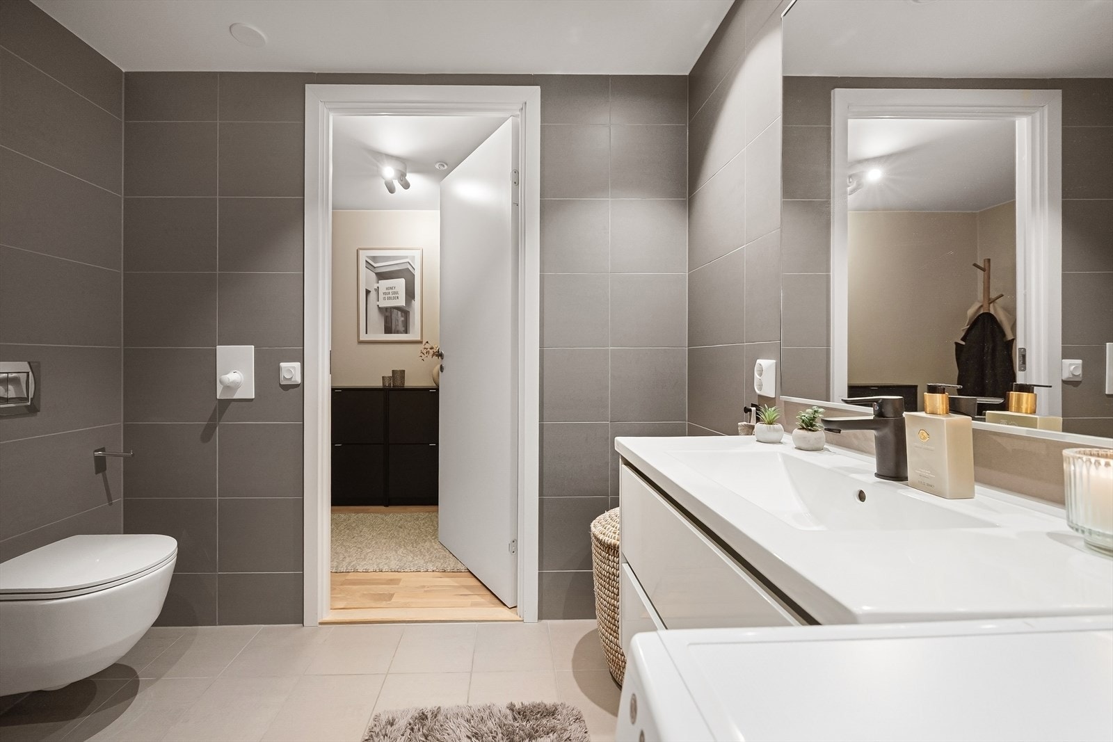 Badet er innredet med servant med speil og dobbel stikkontakt, vegghengt toalett samt dusjhjørne med glassdører og ett-greps armatur med hånddusj. Det er også opplegg for vaskemaskin Galleribilde