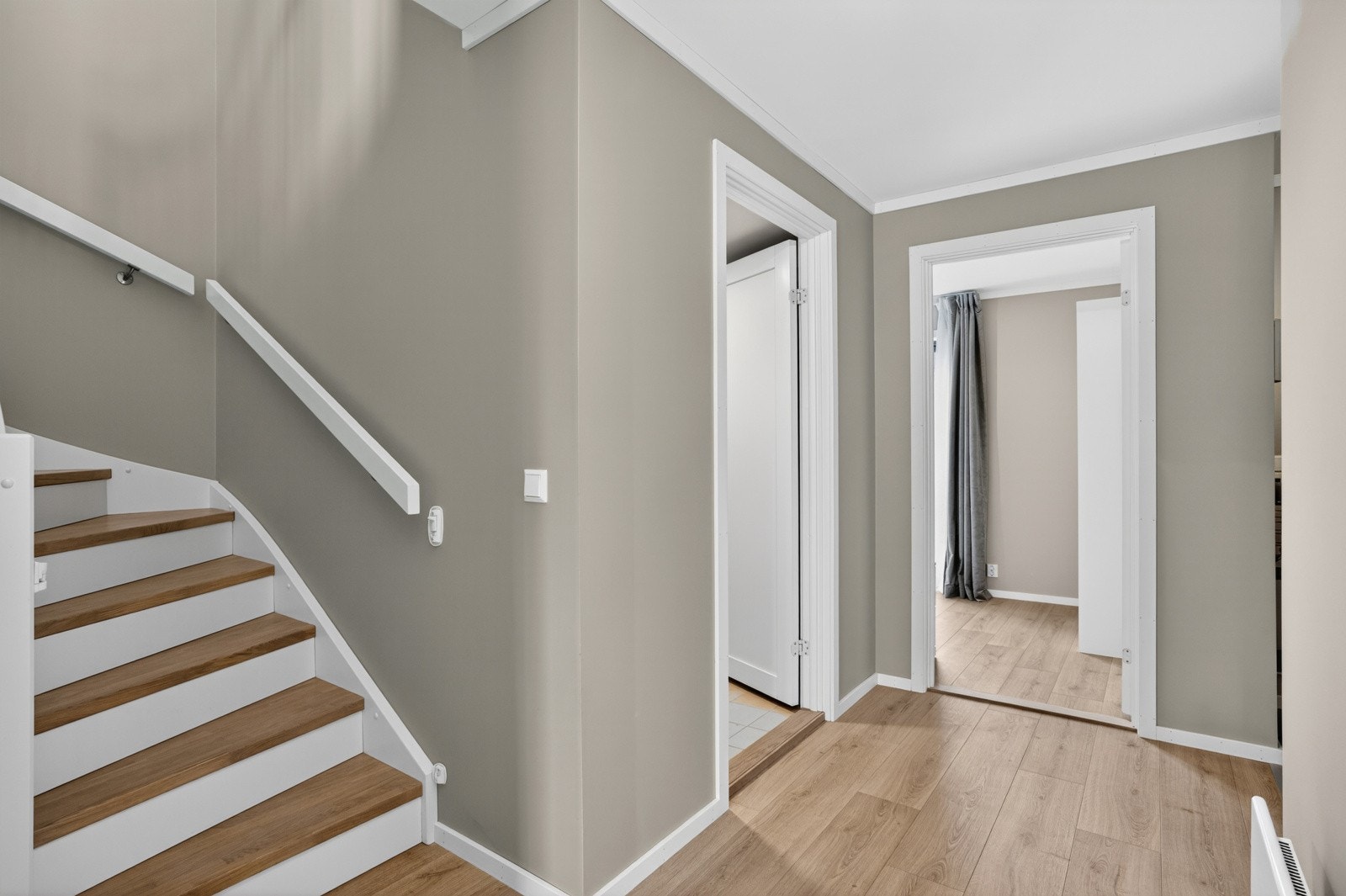 Trappen har malte vanger kombinert med beisede trinn, noe som gir et stilrent og gjennomført uttrykk. Farge- og materialvalget skaper en elegant kontrast og bidrar til å fremheve trappen som et naturlig blikkfang i rommet. Galleribilde
